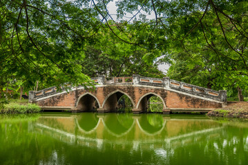 Fototapeta premium Traditional arched brick bridge with green water reflections in Ayutthaya Historical Park