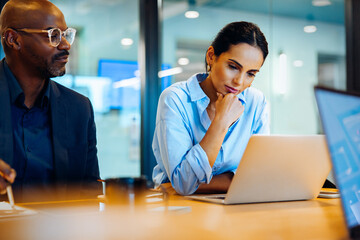 Two adults reviewing documents and discussing ideas while working on laptops