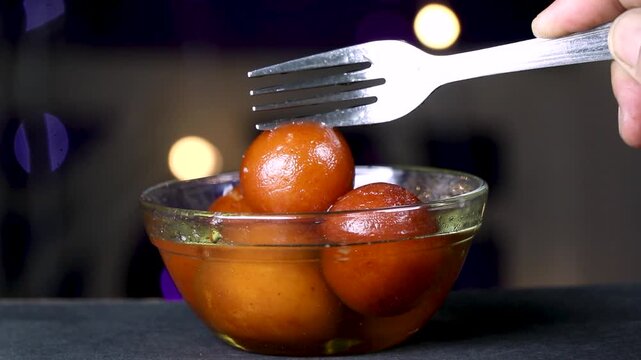 Gulab jamun Indian Sweet or dessert in transparent glass bowl with small glowing bulb in the background.