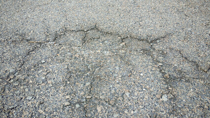 Close-Up of Cracked Gray Asphalt Texture: Deteriorated Pavement Surface with Gravel and Spiderweb Cracks for Infrastructure and Grunge Backgrounds