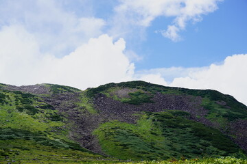 夏雲の下緑と岩肌が広がる広大な山肌を捉えた風景写真です夏山登山のハイキングやトレッキングのイメージとして利用できます