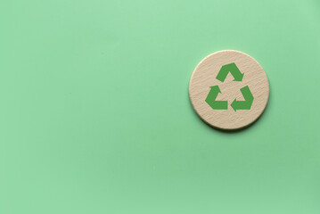 Sustainable Lifestyle Concept: Wooden Coaster with Green Recycle Symbol on Pastel Background Representing Eco-Friendly Living and Environmental Responsibility
