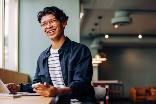 Smiling young man using a laptop and smartphone in a casual setting