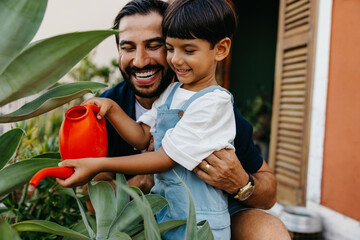 Father and child joyfully watering plants together at home