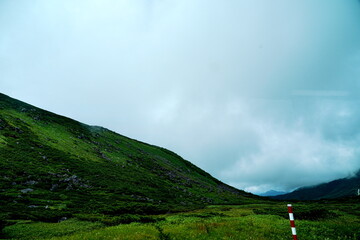 夏曇りの空の下濃い緑の草と岩に覆われた急斜面の山肌が広がる雄大で涼しげな高原の風景写真です
