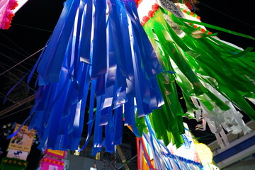 夜空の下で下から見上げるアングルで捉えられた青と緑の紙の短冊が風に揺らめく七夕飾りのクローズアップです