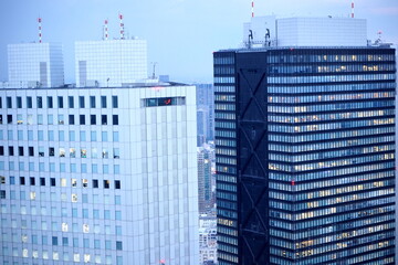 夕暮れ時の都会の空を背景に白と濃紺のツートーンカラーの高層ビルが並び立つ建築とビジネスの風景です