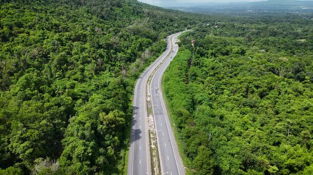 Drone footage of the aerial view of a winding road cutting through lush green forest. Scenic highway number 304 in Thailand links the Bangkok area to Nakhon Ratchasima in the northeastern region