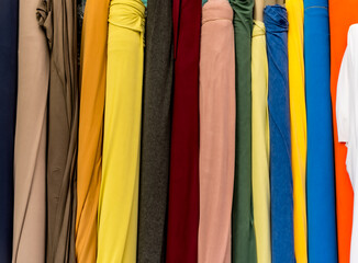 Colorful bolts of fabric neatly arranged in a textile store, showcasing a wide range of materials and shades used in fashion design and garment production, photographed in natural indoor light.
