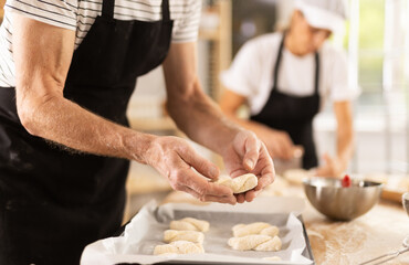 Close-up of baker hands placing pieces of raw dough on baking sheet in oven