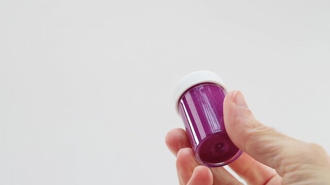 Mano che regge un flaconcino di tempera acrilica di colore viola chiaro, lilla su sfondo bianco - inquadratura ravvicinata