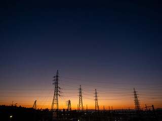 夕焼け空と都市の風景。街並み。鉄塔と電線。オレンジ色から濃紺へのグラデーションの空。日没。横構図。広いコピースペース
