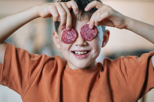 Child playing with salami slices in kitchen while preparing pizza