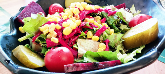 Mix of fresh organic juicy salad greens and red and yellow cherry tomatoes in grey plate on rustic...