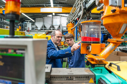 Employees meeting and inspecting machinery in plastics production hall