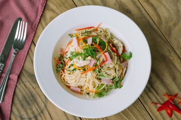 A delicious pasta dish on a plate, featuring ham and fresh vegetables. The spaghetti is artfully arranged with vibrant colors and appetizing presentation
