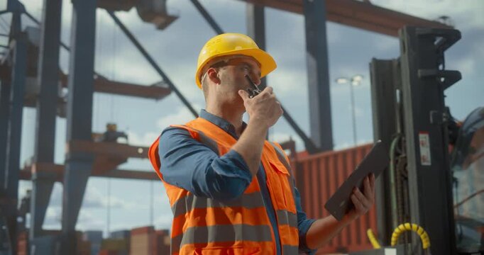 Dock Worker in Safety Gear Uses a Tablet and Radio to Coordinate Cargo Operations at a Busy Port. Cranes Shift Containers,  Logistics and Maritime Product Shimplemtn and Trade.