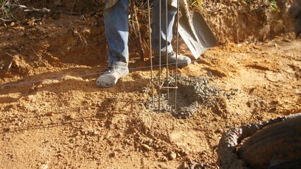 concrete work scene, worker guides concrete mix into prepared hole with rebar reinforcement in rural construction site