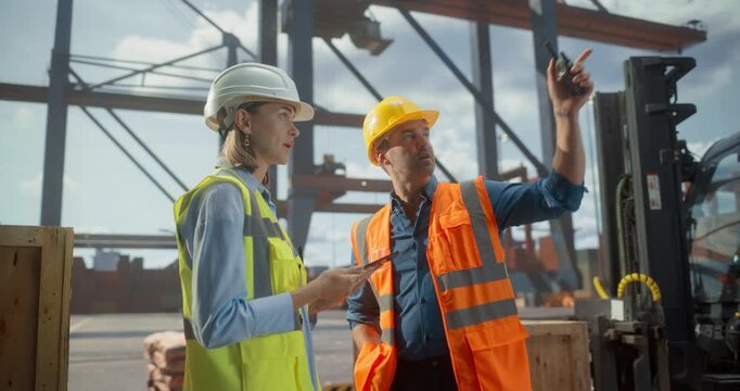 Male Dock Worker and Female Supervisor in Hard Hats and Vests Coordinate Port Logistics With a Tablet and Walkie-talkie. Cargo Container, loading, Unloading with Cranes for furhter Product Shipment