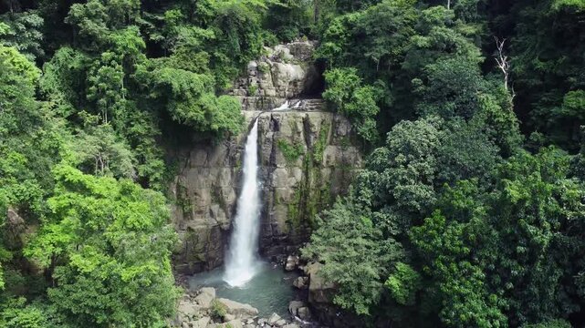 Aerial view of Tomagelli Waterfall cascading down the rocks, surrounded by lush green trees in a tropical landscape, Barru, Sulawesi Selatan, Indonesia.