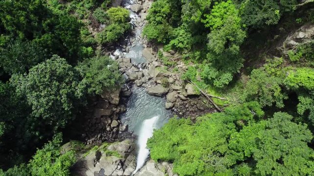 Aerial view of the Tomagelli Waterfall cascading over rocks, surrounded by lush green trees, creating a vibrant scene, Barru, Sulawesi Selatan, Indonesia.