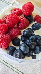 Close-up of fresh raspberries and blueberries served on creamy yogurt in a clear bowl. The image symbolizes freshness, health, and the simplicity of natural breakfast food