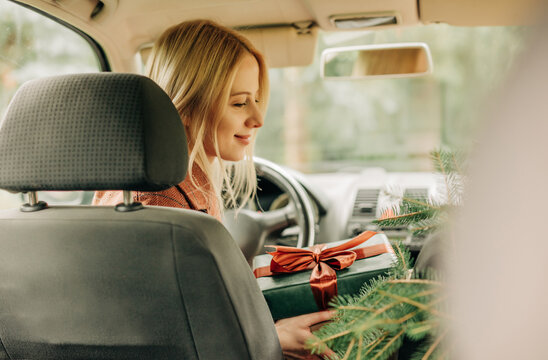 Smiling woman driving car with Christmas gift and festive spirit
