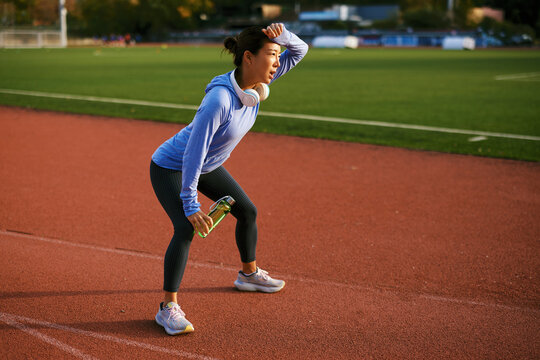 Female athlete resting, wiping sweat from forehead, holding bottle, on a sport track - Powered by Adobe