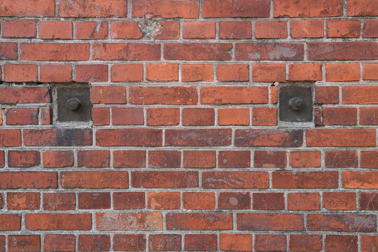 A fragment of an old brick wall of a red brick building. Rusted fastening nuts of the interior floors are visible. Background. Texture.