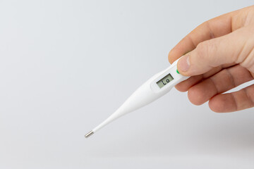 Hand holding a digital thermometer displaying a temperature reading, showcasing a health monitoring tool against a clean, minimalistic background emphasizing wellness and care