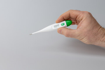 Hand holding a digital thermometer displaying temperature reading, showcasing healthcare technology and personal health monitoring in a clean, minimalistic environment