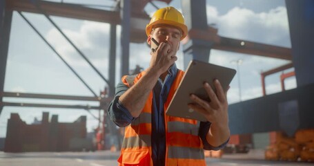  Male Logistics Worker in Safety Gear Uses a Tablet and Radio to Streamline Container Operations at a  Port, Optimizing Shipping Processes Amid Cranes and Cargo.