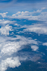 Expansive aerial view of fluffy white clouds drifting above the landscape, with faint details of mountains and land patterns visible beneath, capturing the calm beauty and vastness of the sky from hig