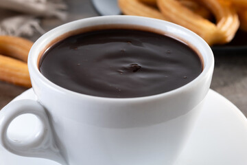 Hot thick chocolate in a white cup with churros on wooden table