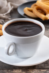 Hot thick chocolate in a white cup with churros on wooden table