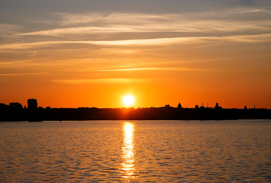 A sunset at the Kiel Fjord on the Baltic Sea with silhouettes of houses on the horizon.