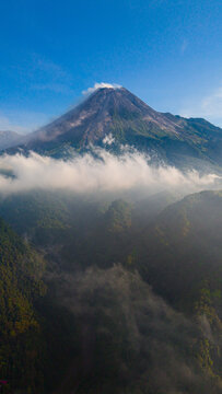 Aerial view of the majestic Merapi Mountain piercing through a sea of clouds, its peak capped with a wisp of smoke, Yogyakarta, Daerah Istimewa Yogyakarta, Indonesia.