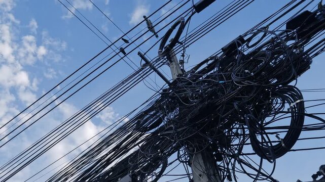 Messy tangled electrical power cables and wires on utility pole against blue sky showing chaotic infrastructure