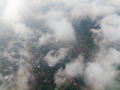 Aerial view of a landscape shrouded in a blanket of white clouds, partially obscuring the green terrain below, Kaliurang, Daerah Istimewa Yogyakarta, Indonesia.