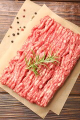Raw minced meat with peppercorns and rosemary on wooden table, top view