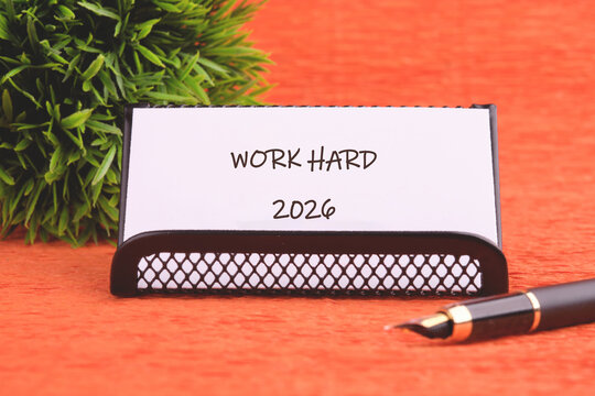 A motivational note stands in a stylish holder, reminding viewers to work hard in their pursuits. A pen lies nearby, ready for ideas and goals. A green plant adds life to the scene