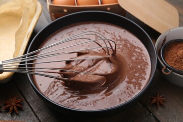 Mixing liquid chocolate dough with whisk in bowl at wooden table, closeup