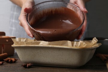 Woman pouring liquid chocolate dough into baking dish at wooden table, closeup