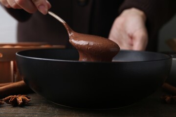 Woman mixing liquid chocolate dough with spoon in bowl at wooden table, closeup