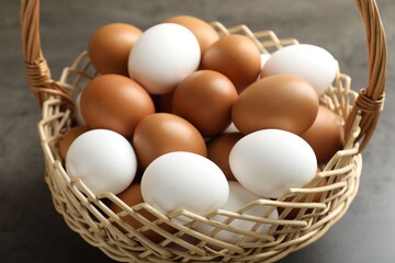 Raw chicken eggs in wicker basket on grey table, closeup