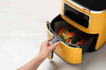 Woman opening air fryer with grilled vegetables at white wooden table, closeup. Space for text
