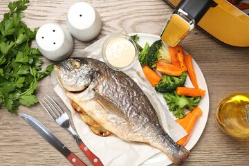 Tasty grilled fish, vegetables, sauce and air fryer on wooden table, flat lay
