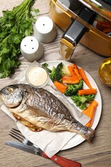 Tasty grilled fish, vegetables, sauce and air fryer on wooden table, flat lay