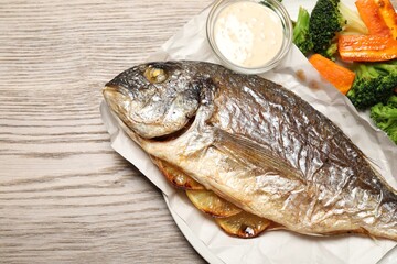 Tasty grilled fish, vegetables and sauce on wooden table, top view. Space for text