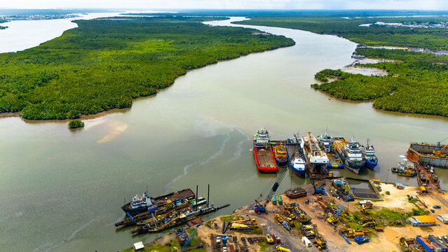 Aerial view of ships clustered at the Abuloma Jetty, where the river meets the land, a vibrant contrast of industrial activity and untouched nature, Port Harcourt, Rivers State, Nigeria.